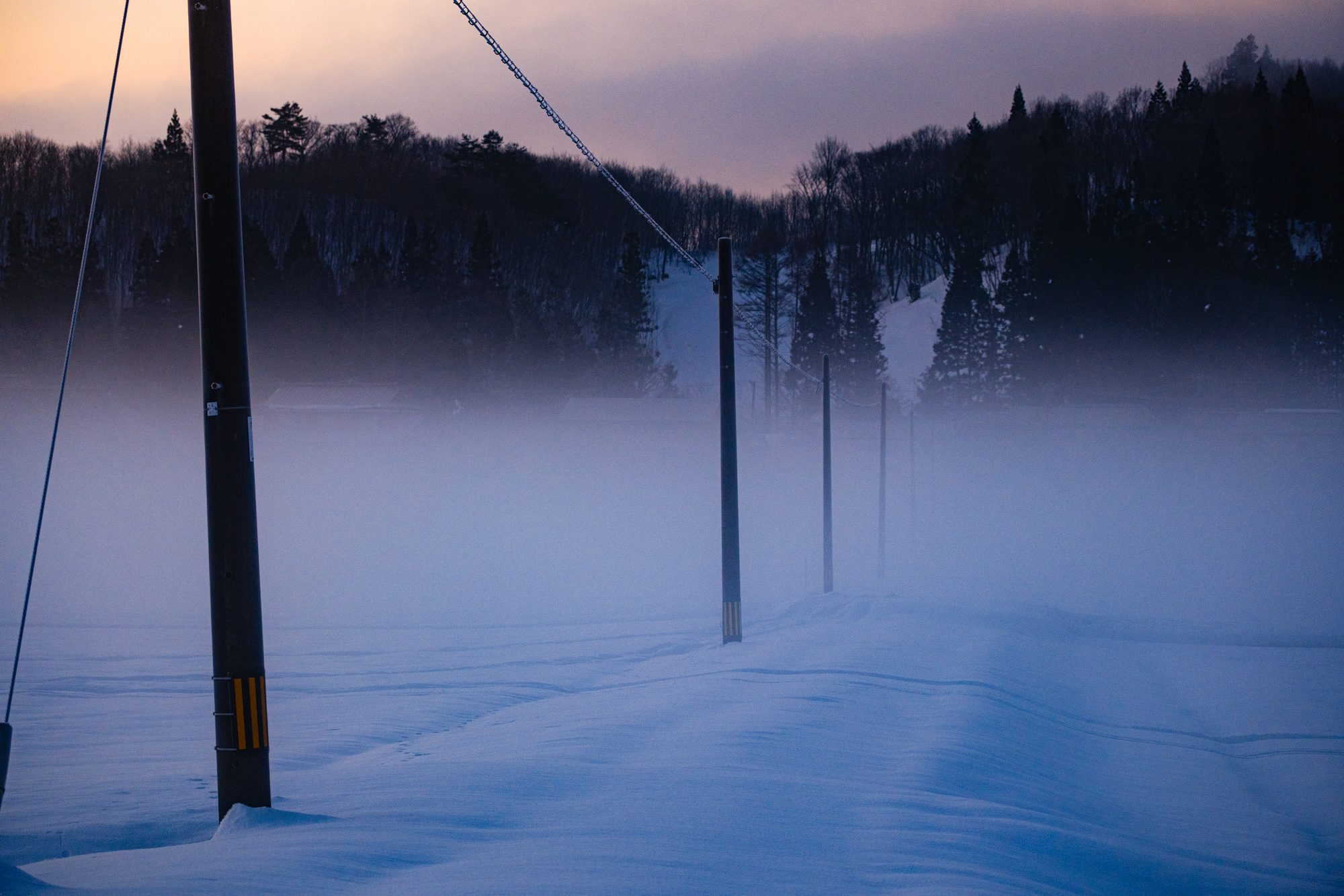 雪原霧靄，列桿沒入遠方，天際一線暖光